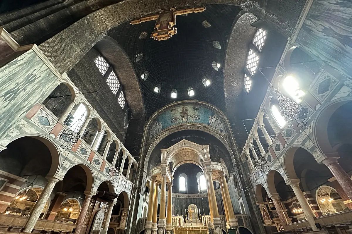 Looking up inside the cathedral at a dark brick dome pierced by small windows, above striped marble arcades and a high arch.