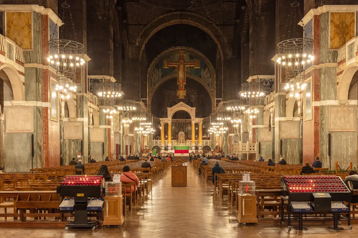 The long nave of Westminster Cathedral seen from the entrance, with hanging lamps, striped arcades and the great Rood cross above the sanctuary.