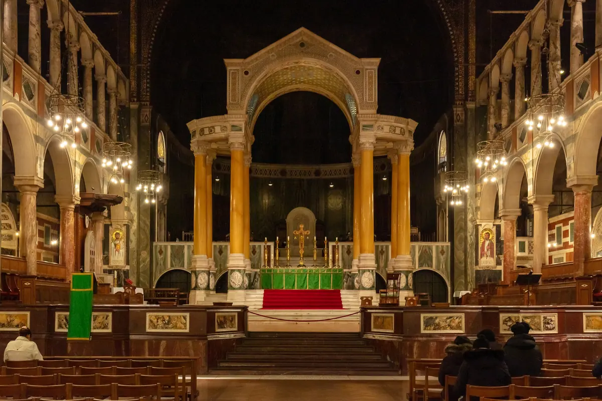 The sanctuary of Westminster Cathedral, with yellow marble columns holding up the baldacchino over the high altar, arcades on both sides and a dark apse behind.