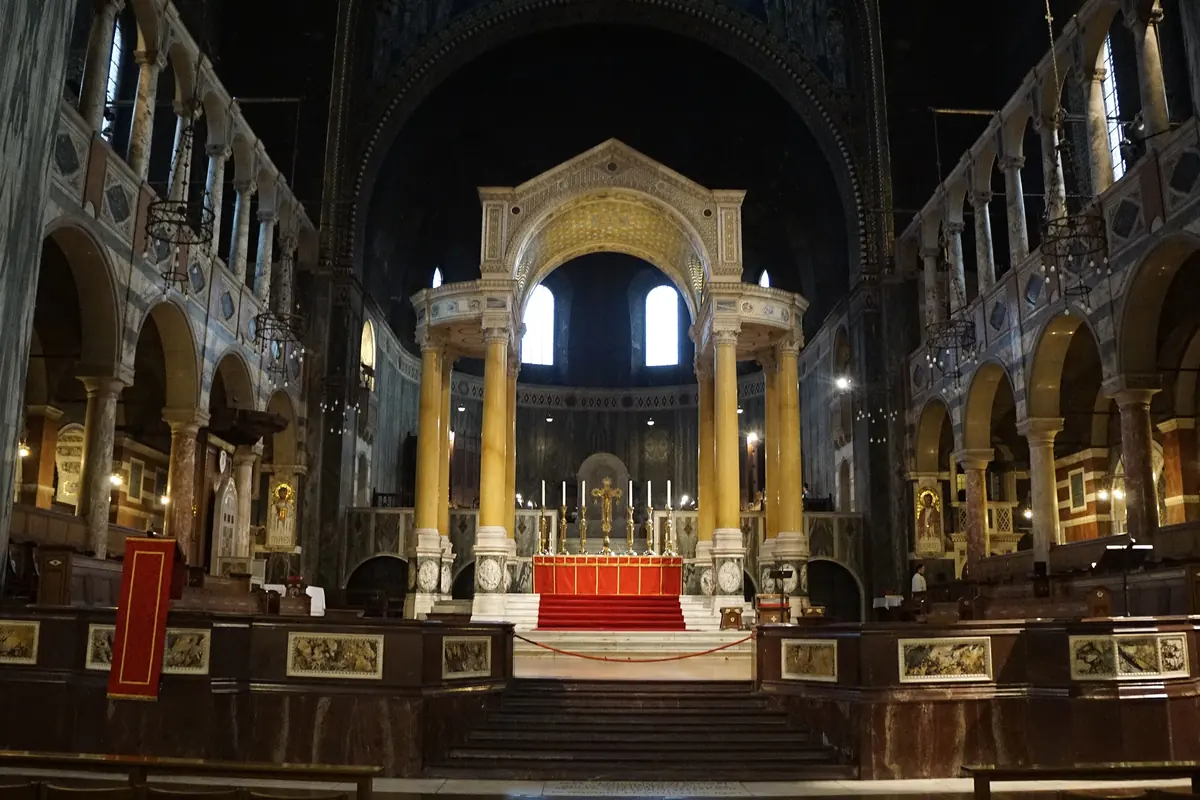 The sanctuary of Westminster Cathedral seen from the nave, with the yellow marble columns of the baldacchino framed by arcades and a dark arch above.